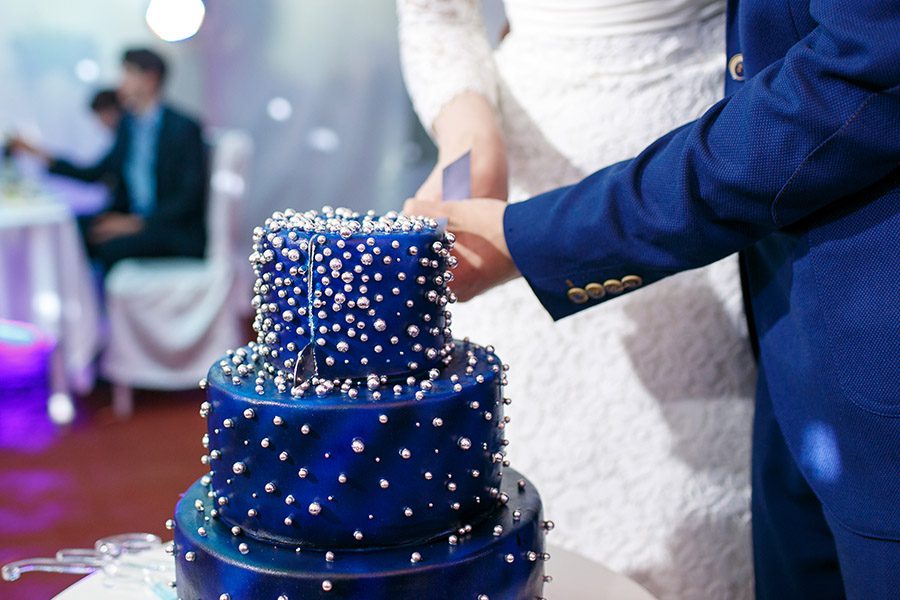 Blog - A Close-up of a Bride Wearing a White Dress and Groom Wearing a Blue Tuxedo Cutting a Blue Wedding Cake