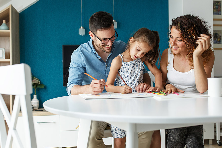 Personal Insurance - A Happy Mother and Father are Sitting at a Table With Their Daughter Drawing Pictures on Paper at Home