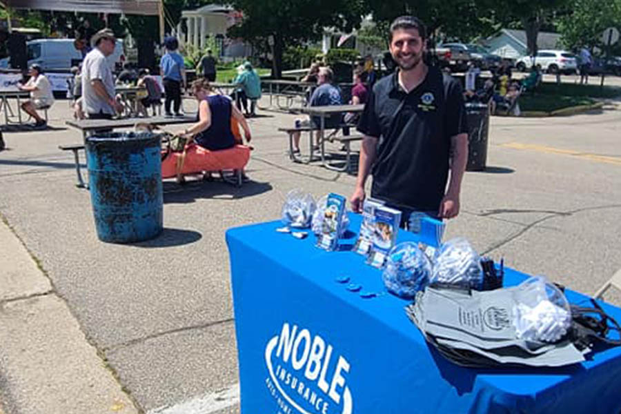 Community Involvement - Noble Insurance Team Member Standing at a Stand